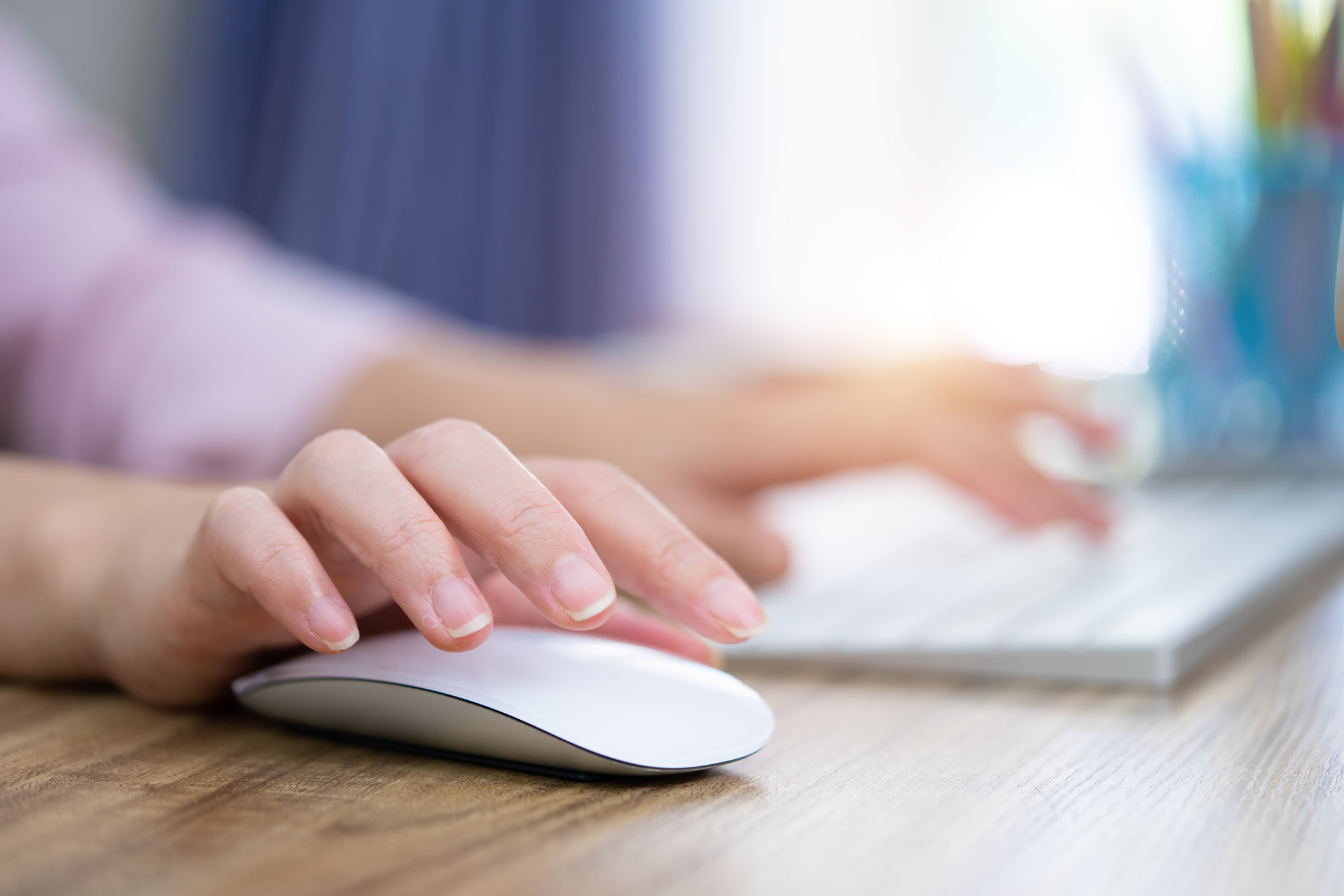 Hands hovering over a white computer keyboard and mouse. 