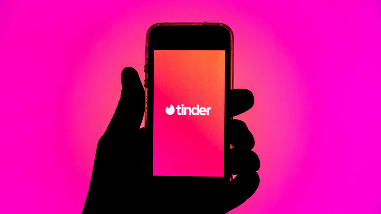 An iPhone featuring the Tinder logo, against a pink background.