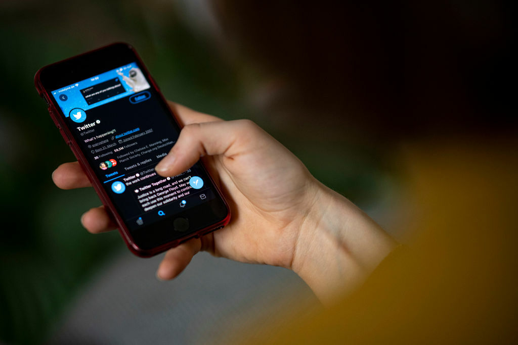 Hand holding a smartphone displaying the Twitter app.