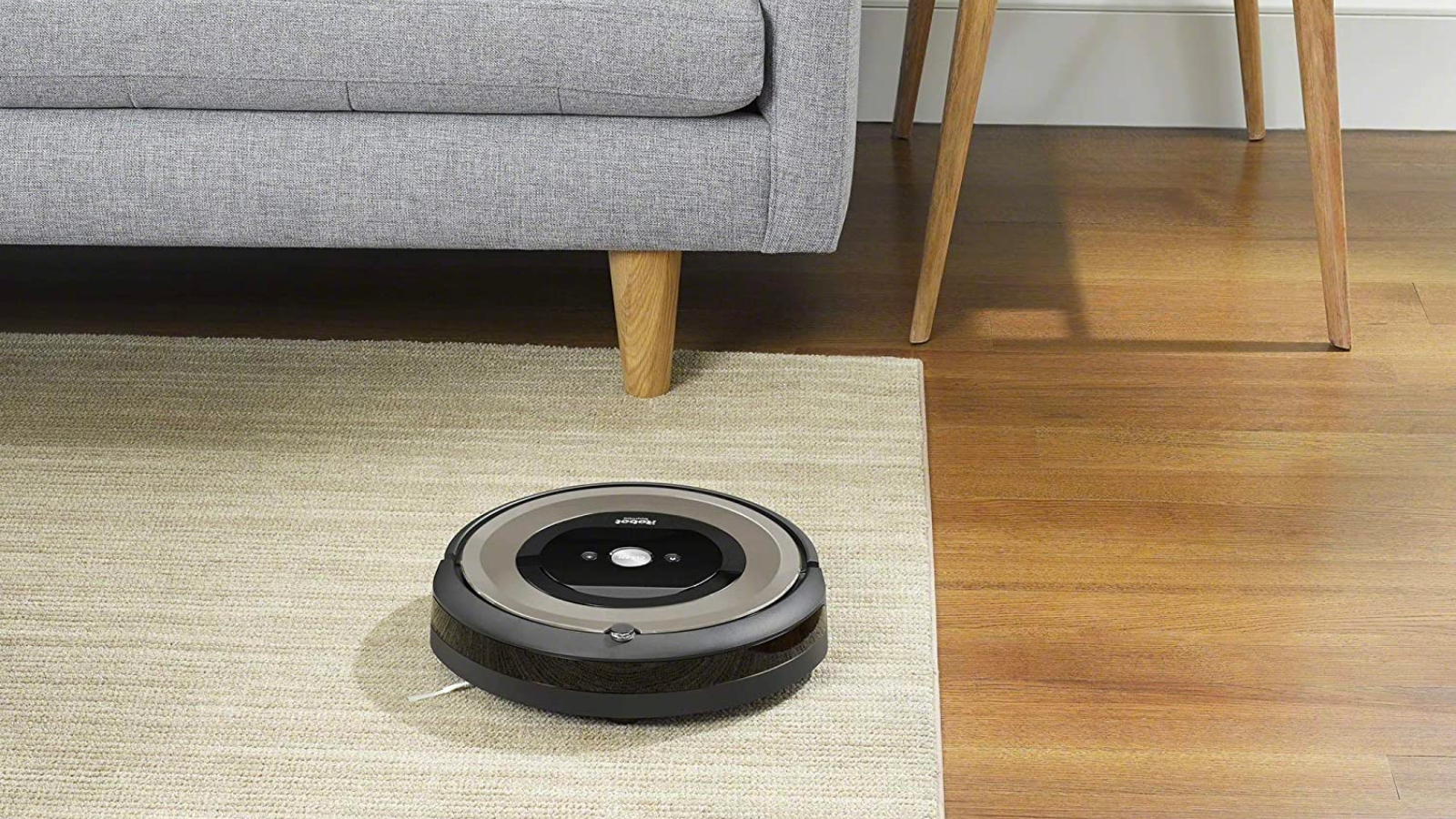 a roomba vacuuming a rug next to a couch and a wooden end table