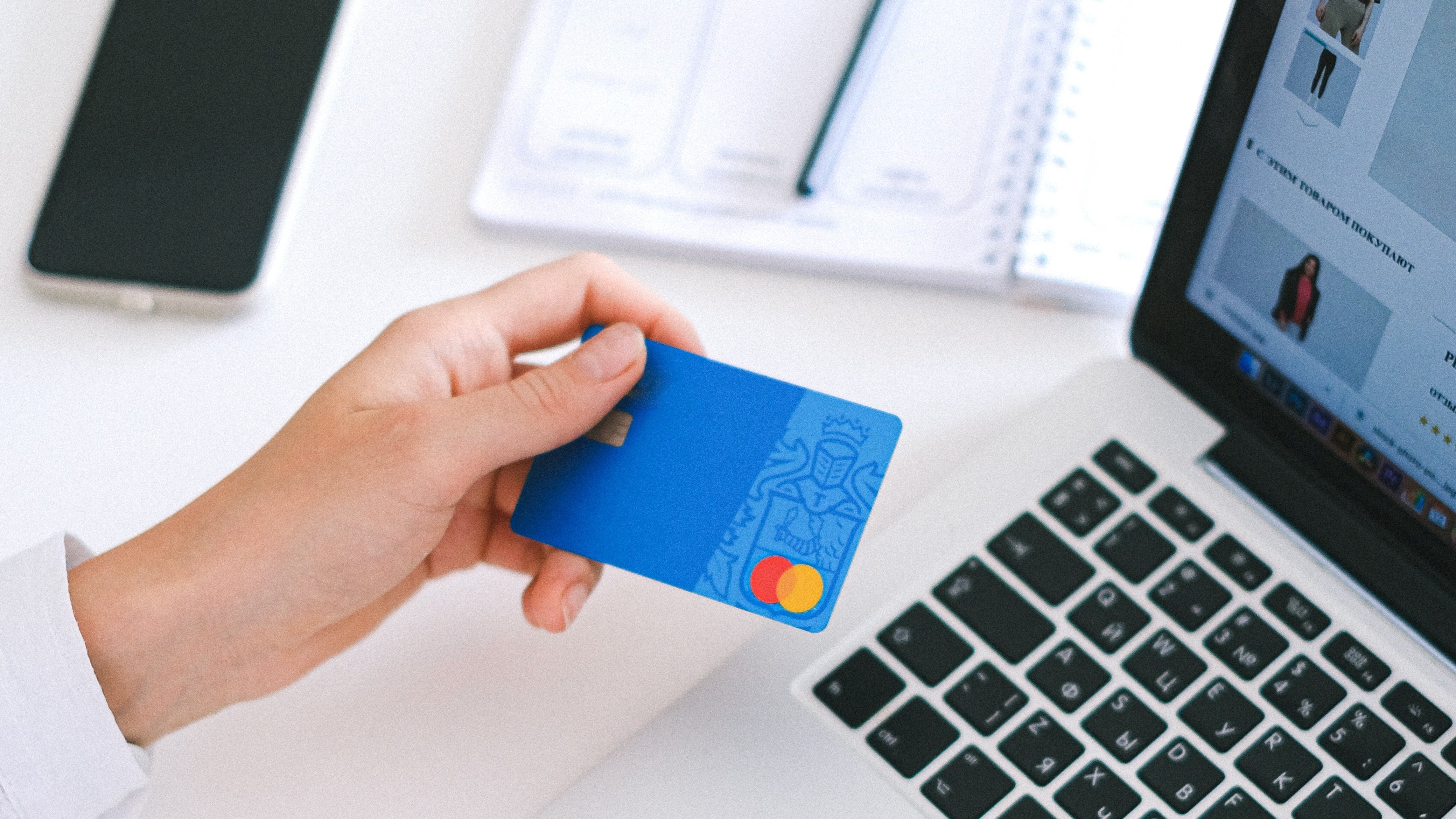 Hand holding blue credit card in front of laptop