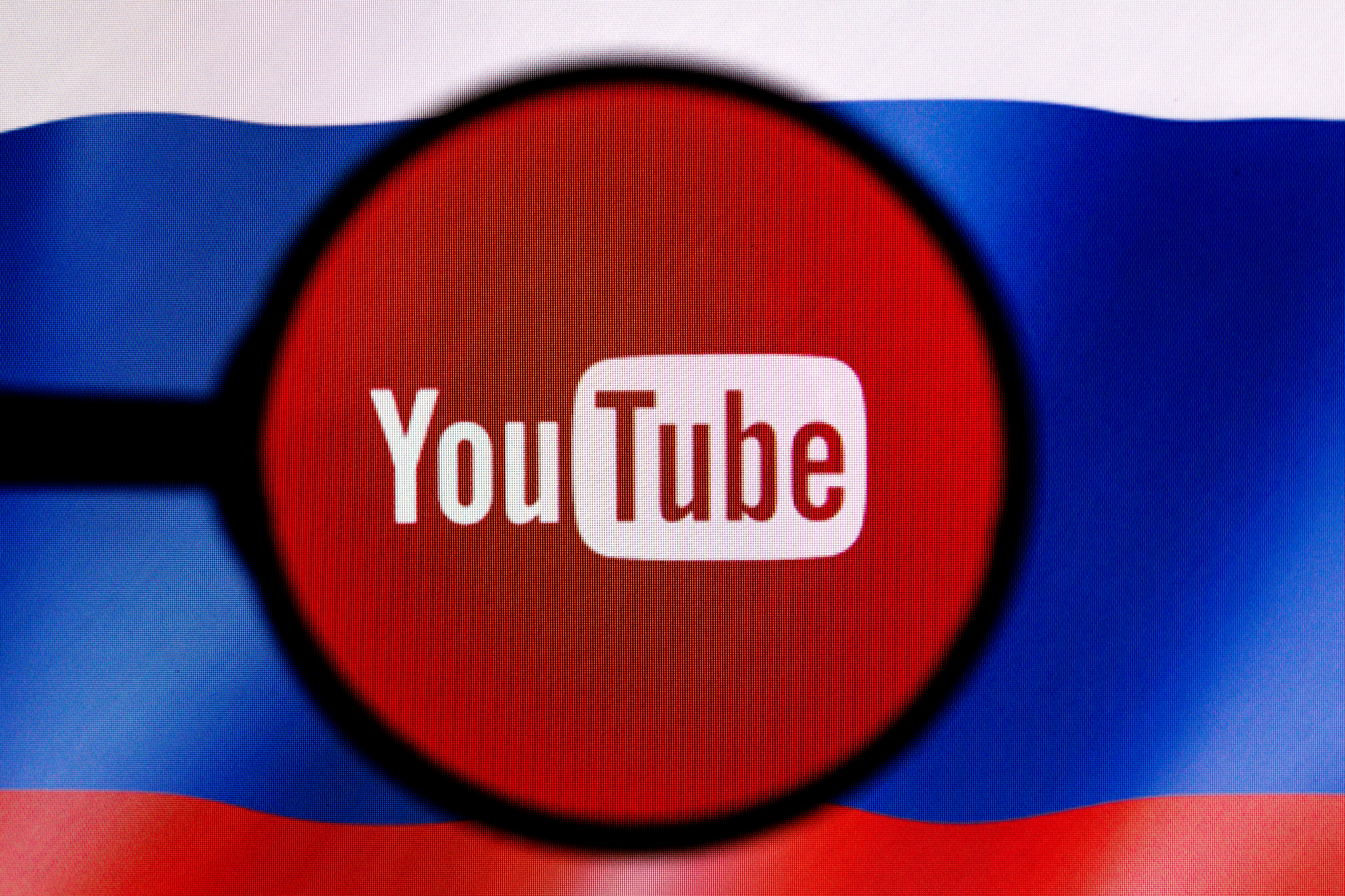 The YouTube logo appears through a magnifying glass held over a Russian flag.