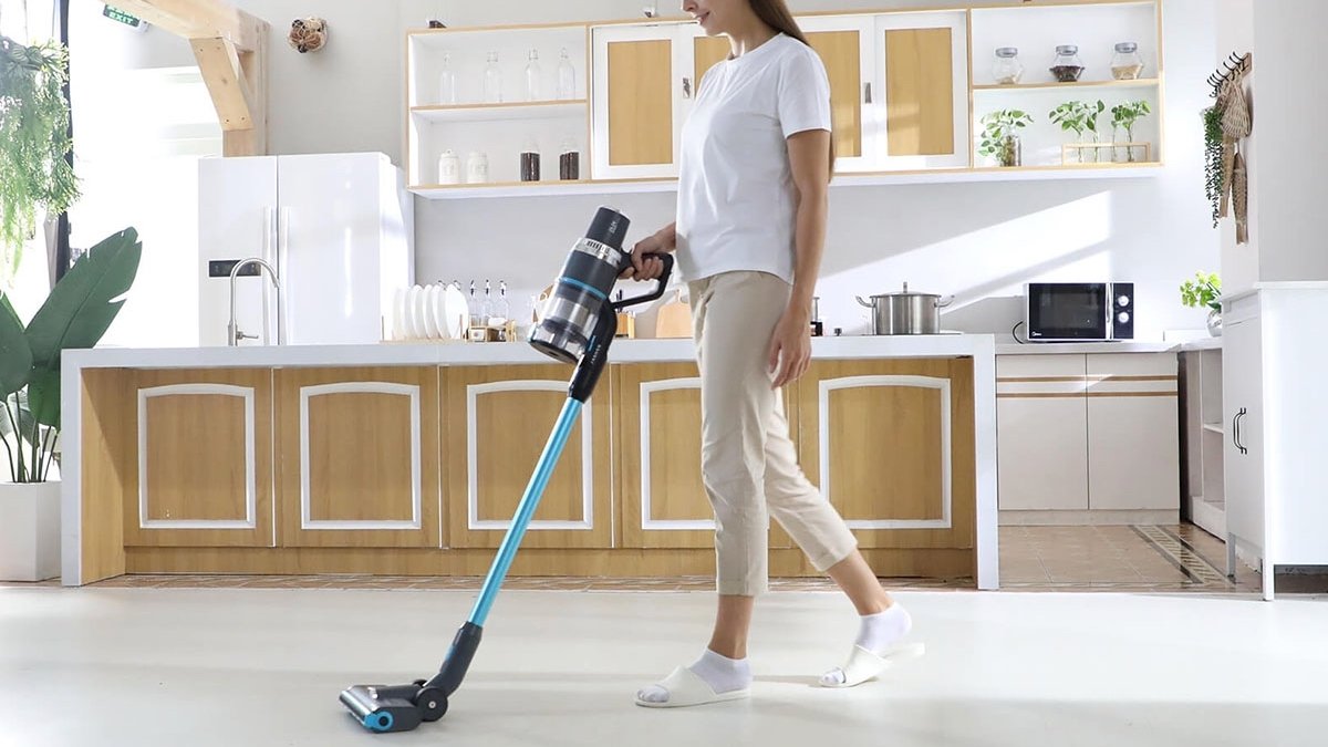 Person using blue cordless vacuum cleaner to clean white floor in kitchen