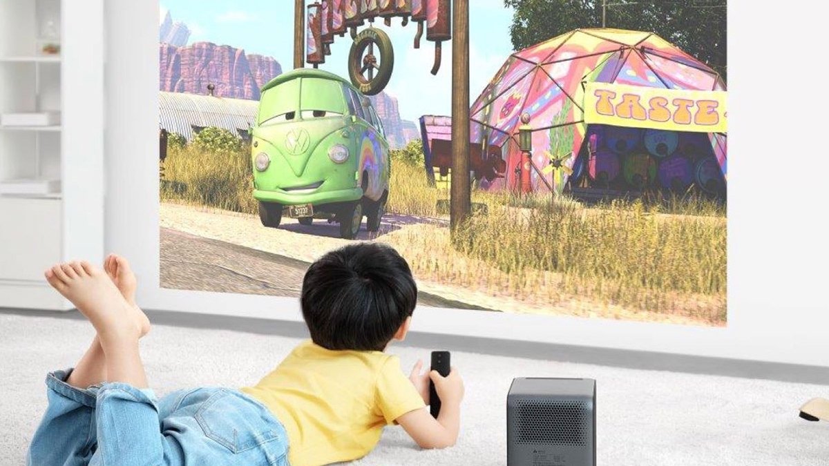 Child lying on stomach watching cars on wall as projected by black cube next to child