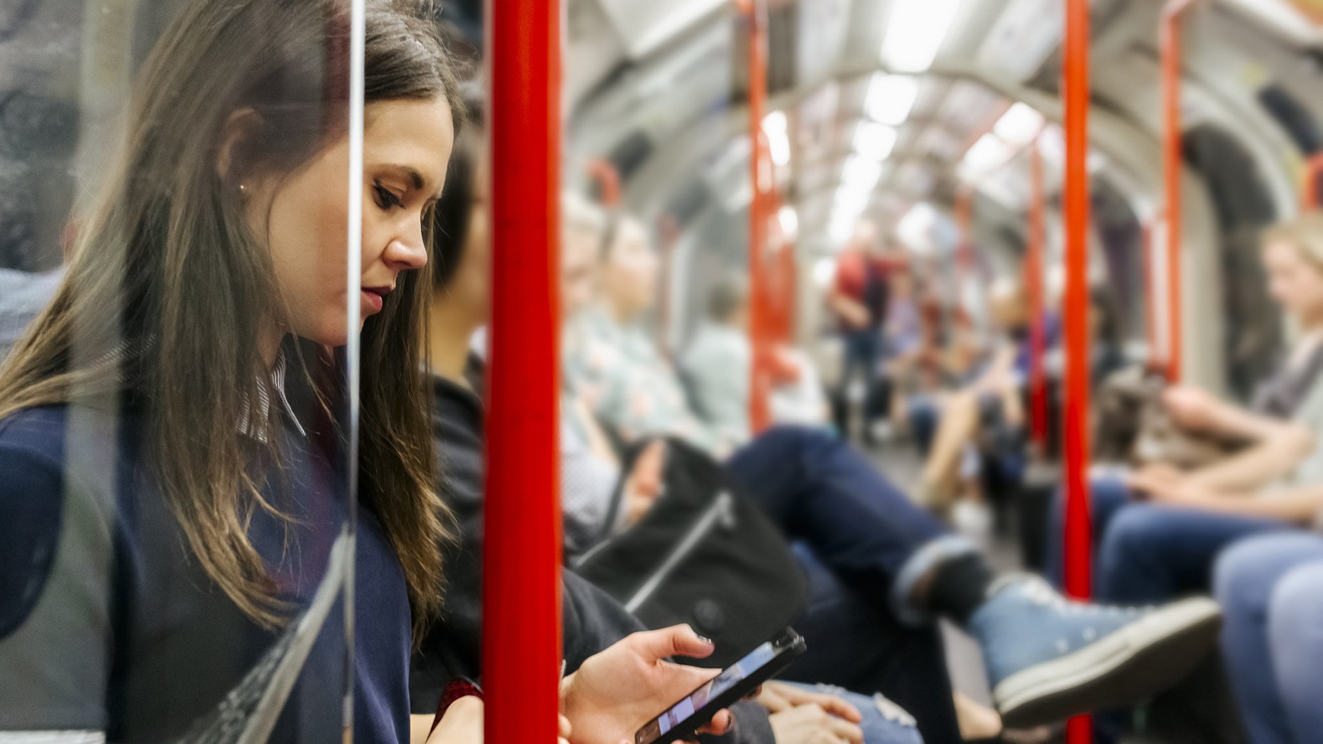 Woman sits on the London Underground looking at a phone in her hand. 