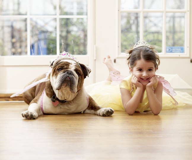 Image of little girl and bulldog, both wearing tiaras, lying next to each other