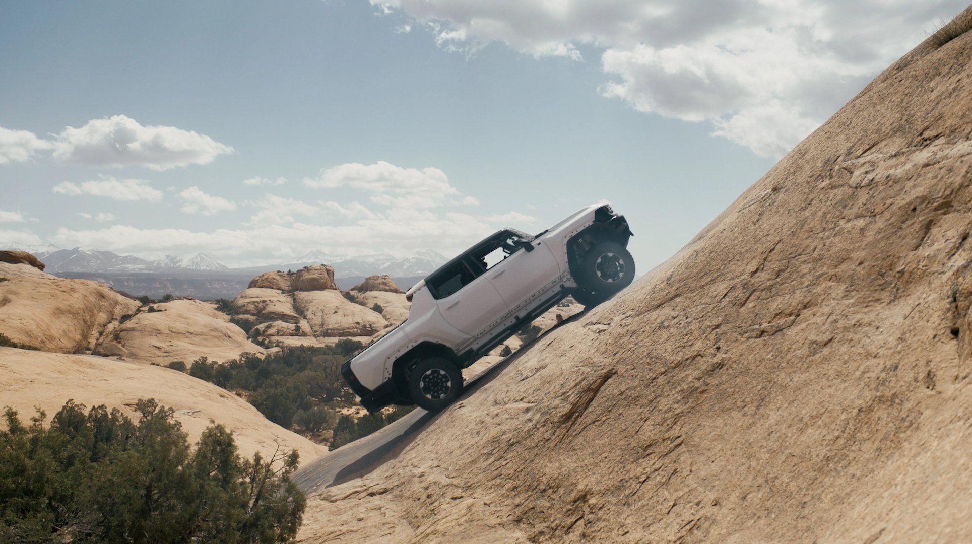 A white Hummer EV climbs up a steep desert hill.