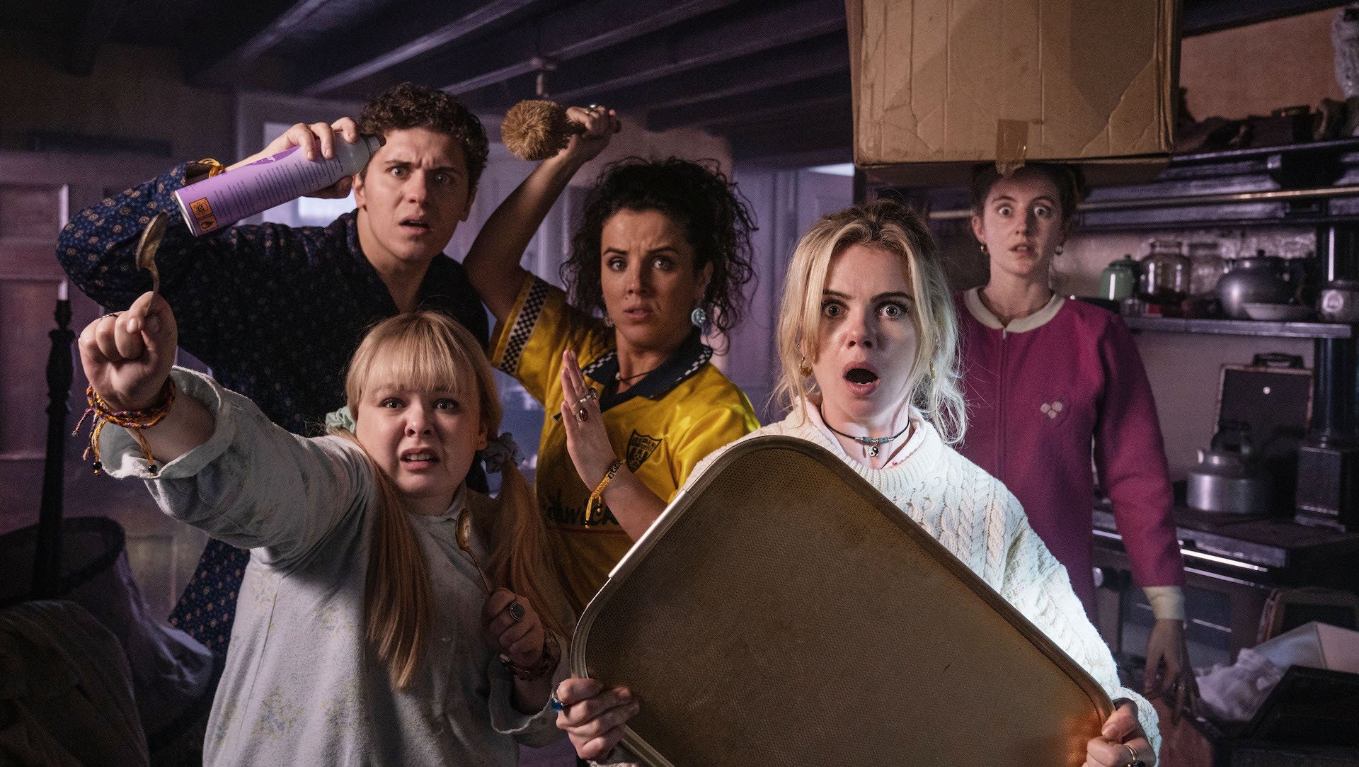 The cast of Derry Girls look at the camera looking horrified and brandishing kitchen implements as weapons.