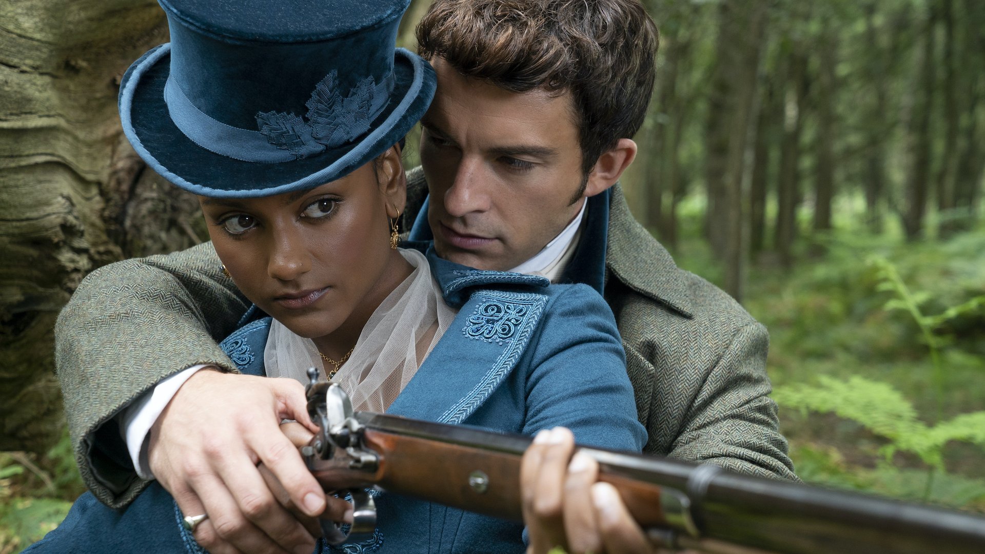 A man helping a woman in a teal top hat adjust her grip on a rifle; still from 