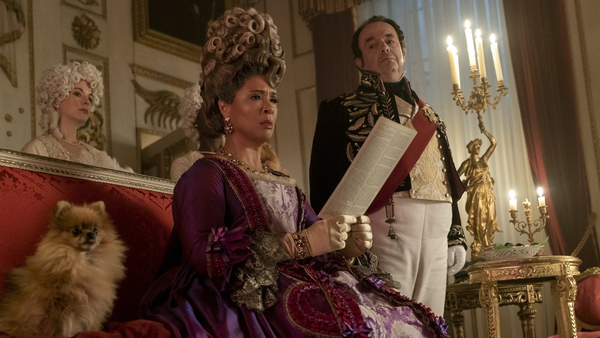 A Regency Queen reads a piece of paper while flanked by a guard and sitting next to her perfect fluffy dog; stlil from