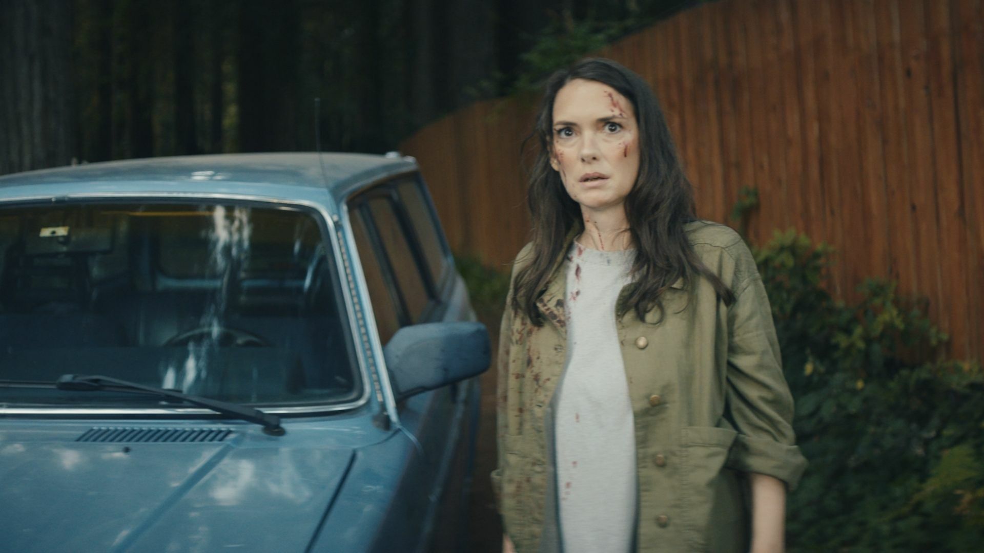 A middle-aged woman splattered with blood looks shocked. 