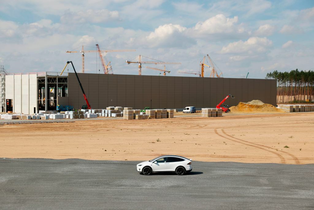A white car in front of a partially finished Tesla factory.