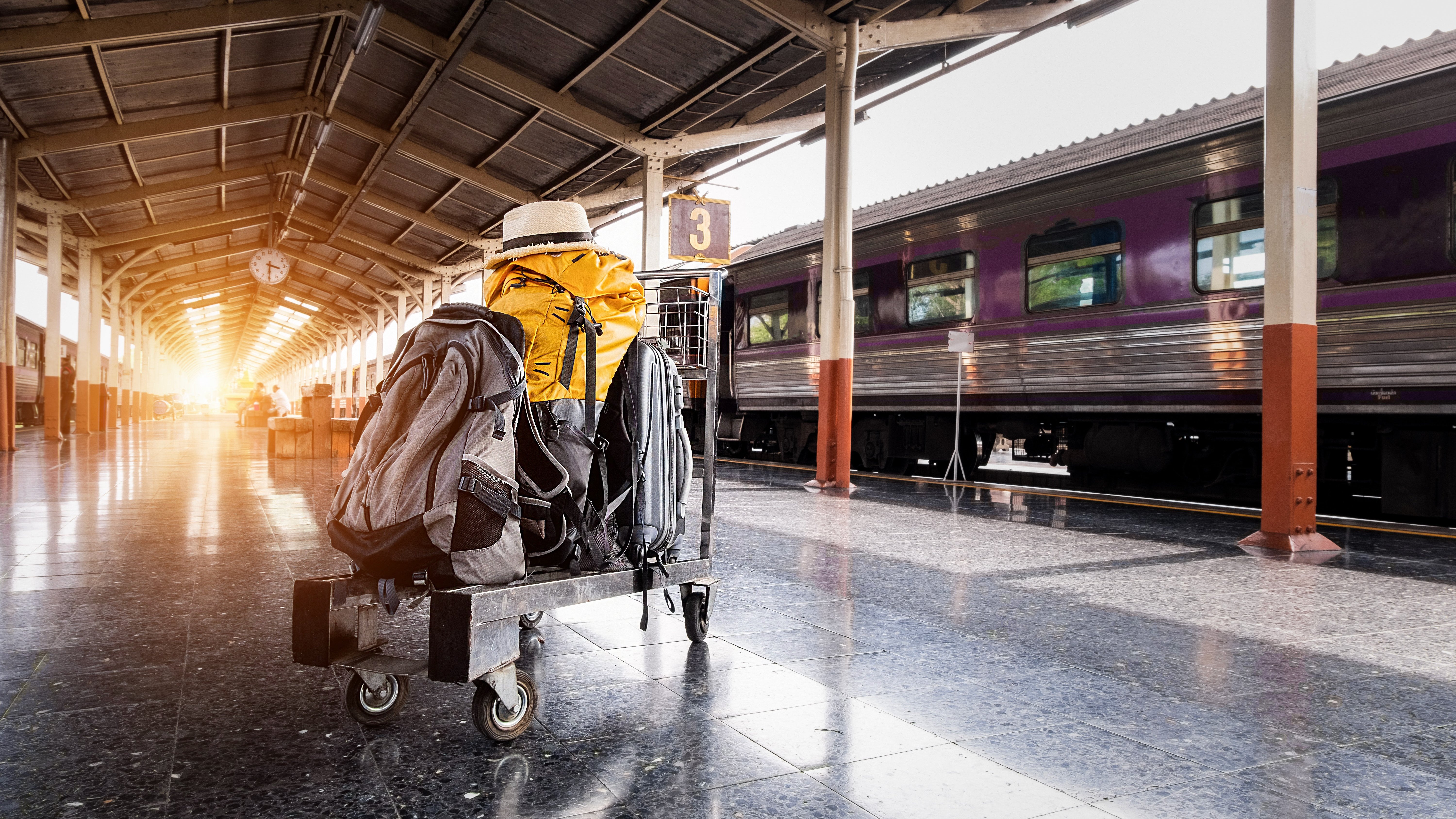 Backpack, suitcase, and hat on luggage trolley on train platform