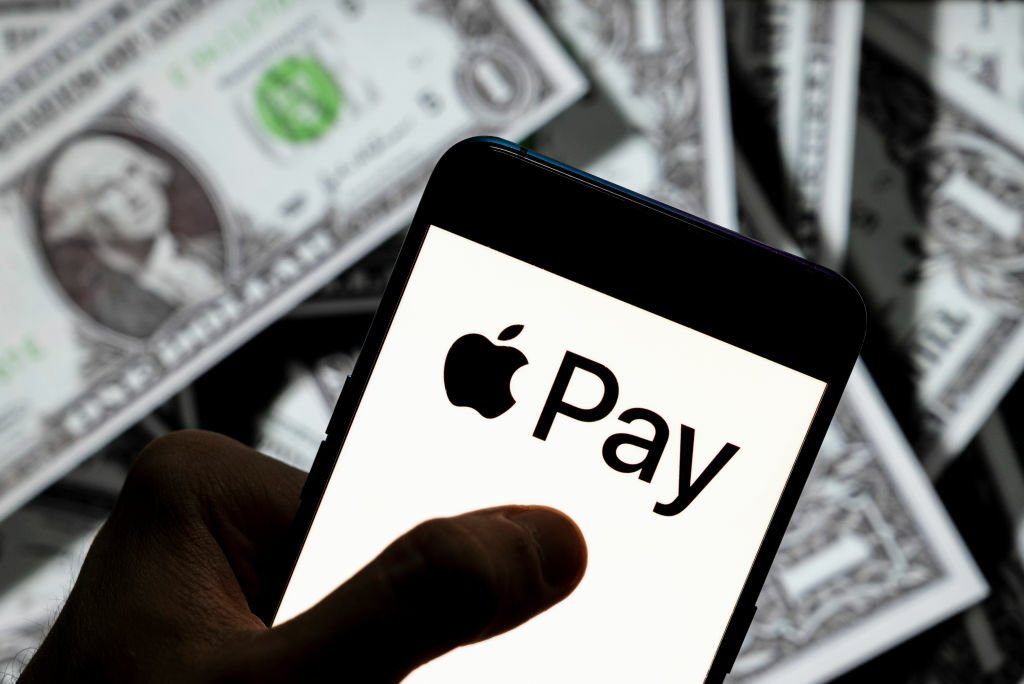 A smartphone, displaying the Apple Pay logo, held in front of cash.