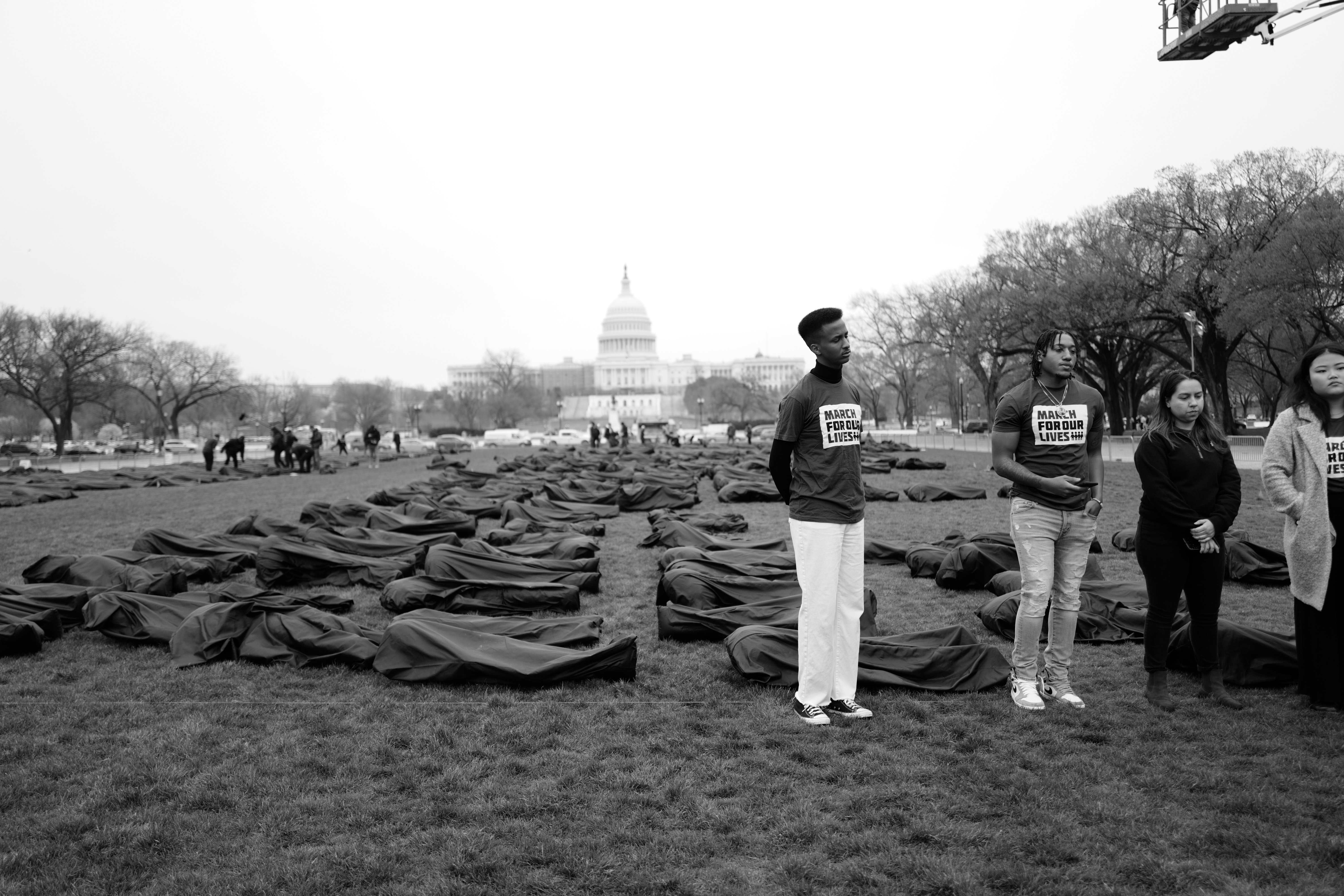 Four activists stand next to body bags laid out on the National Mall.