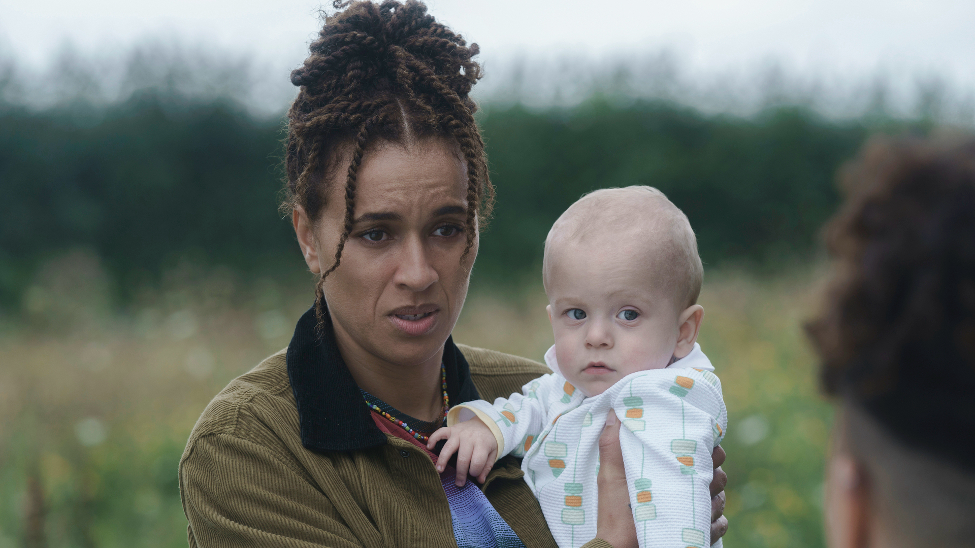 A woman holds a baby in a field.