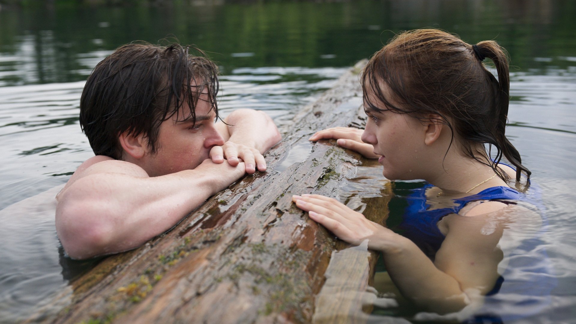 Ferdia Walsh-Peelo and Emilia Jones in facing each other in the water, holding onto a log, in “CODA,” on Apple TV+.