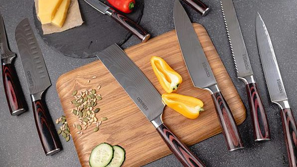 Set of silver knives on top of cutting board with peppers and other cut-up food