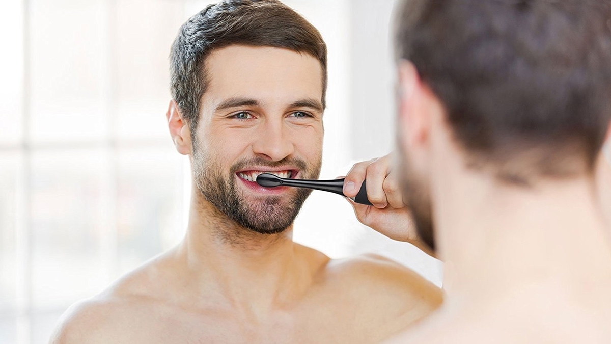 Person looking into mirror and smiling while brushing teeth with black toothbrush