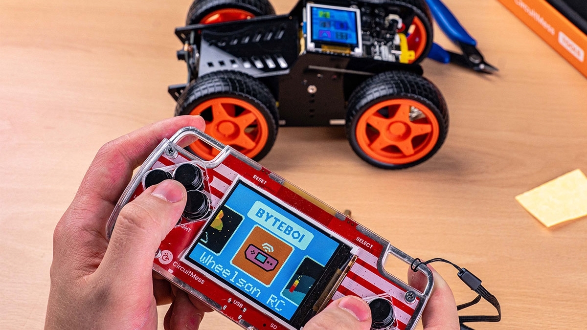 Hands on red game console with toy car in background