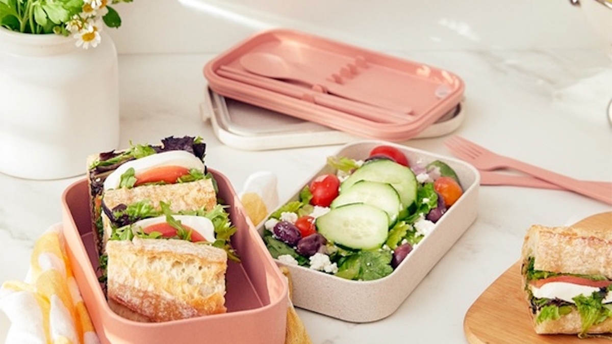 Pink and white lunch boxes filled with sandwiches and salad