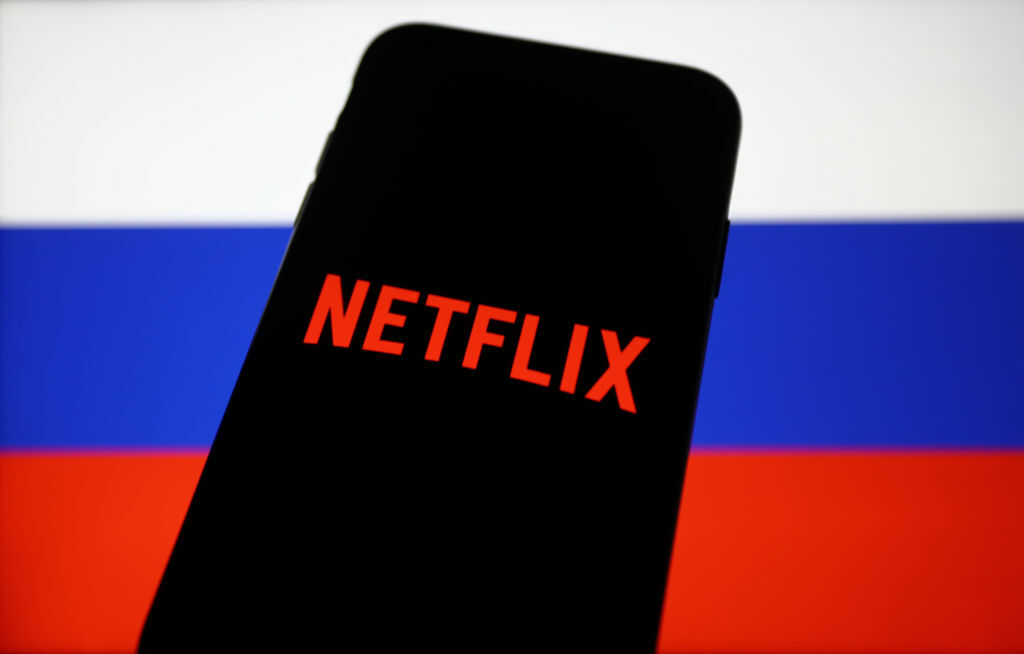 Netflix logo displayed on a phone screen and Russian flag displayed on a screen.