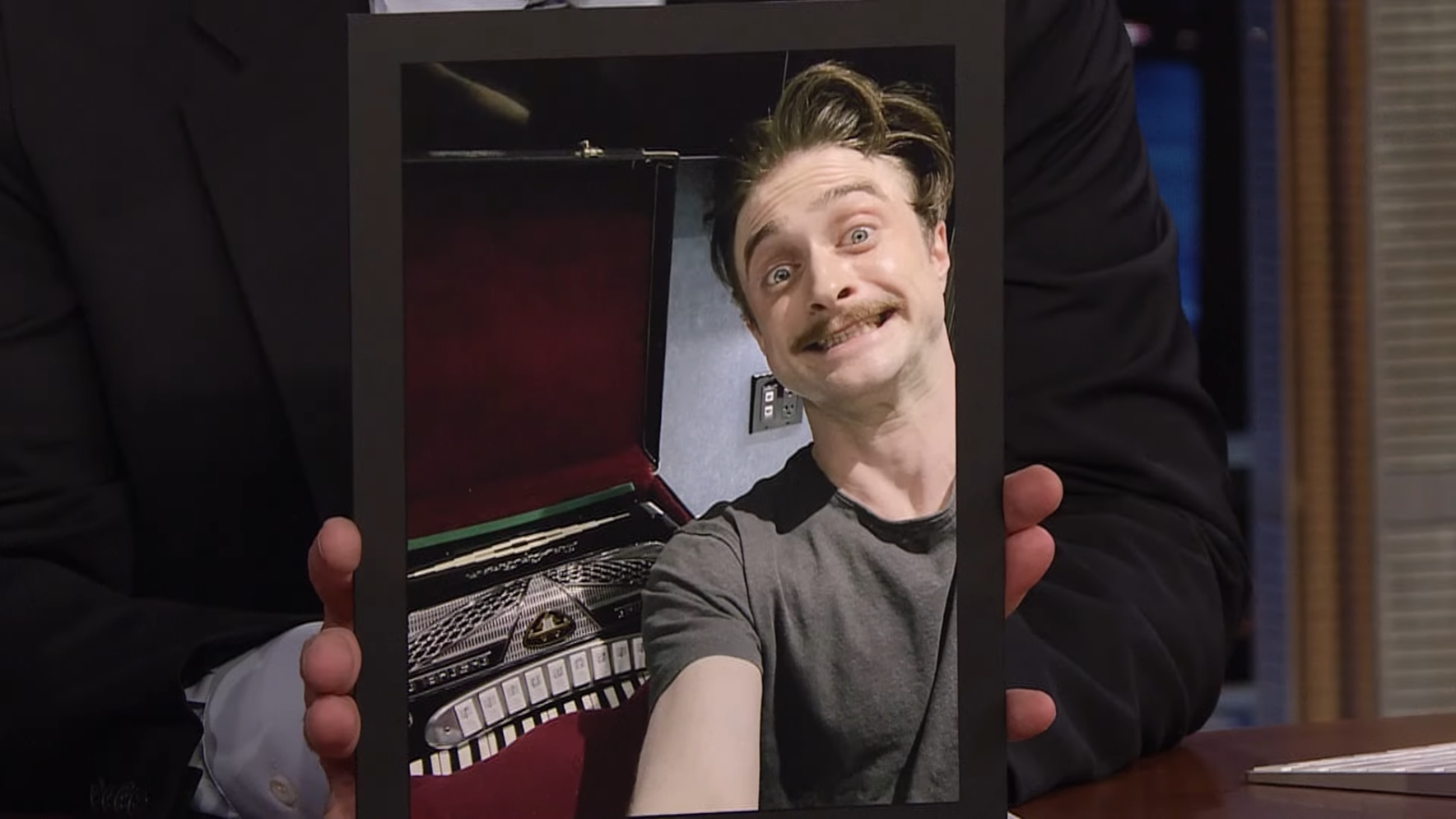 Someone holding a photo of a smiling Daniel Radcliffe posing next to an accordion that belongs to