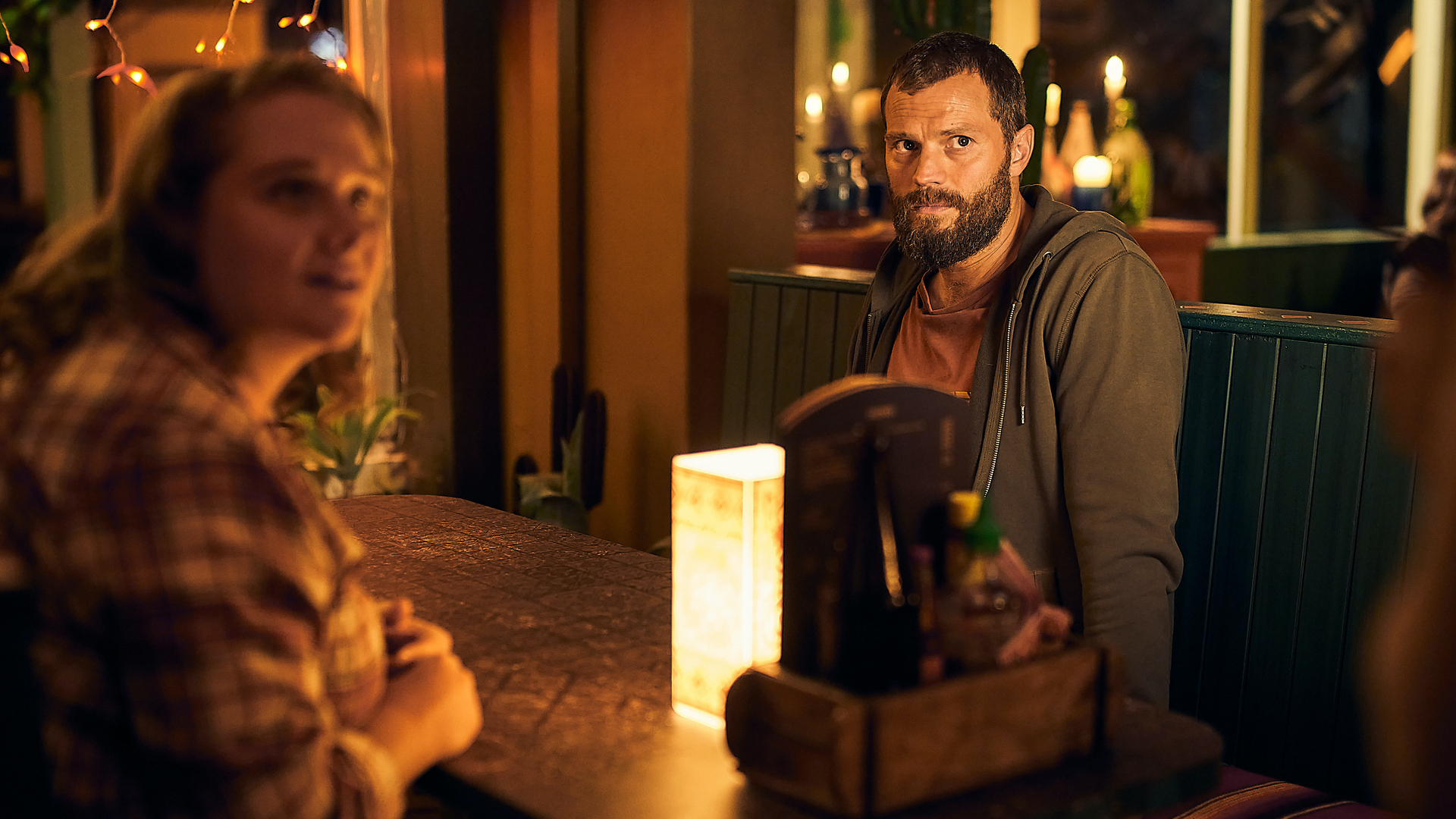 A man and woman sit at a restaurant table, looking alert; a still from "The Tourist."