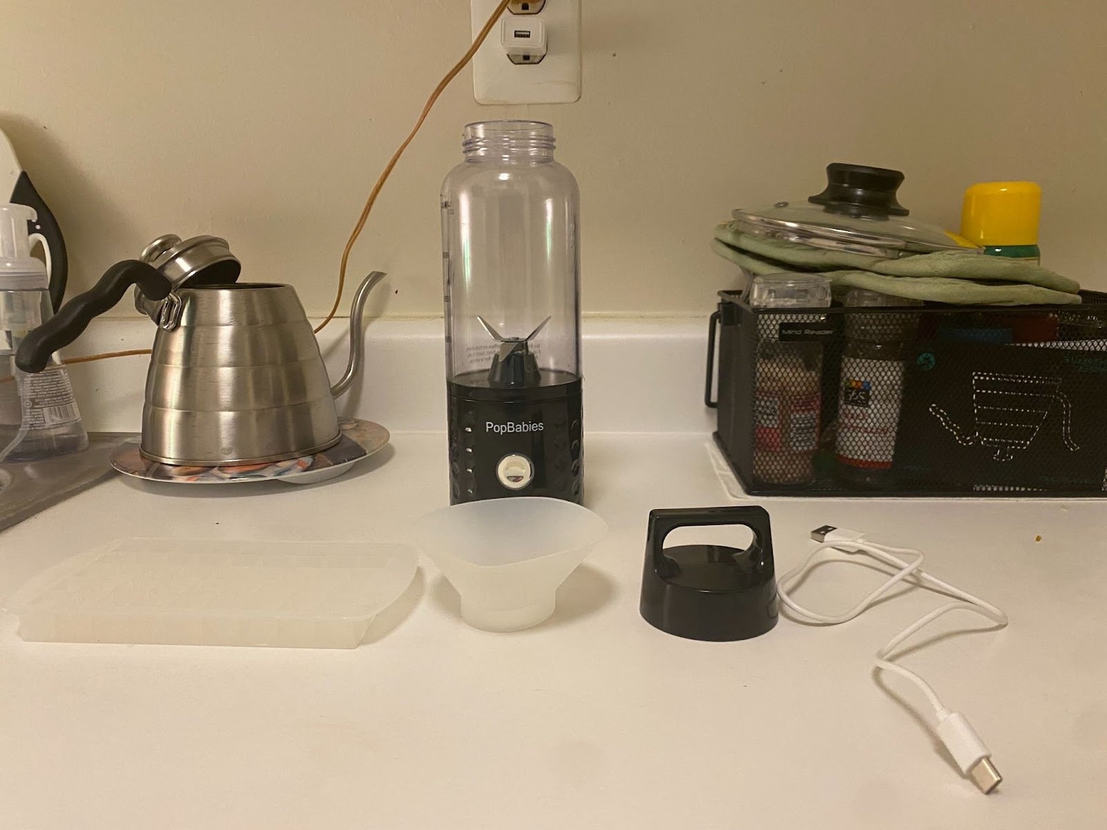 blender, ice tray, funnel, lid, and charger laid out on counter