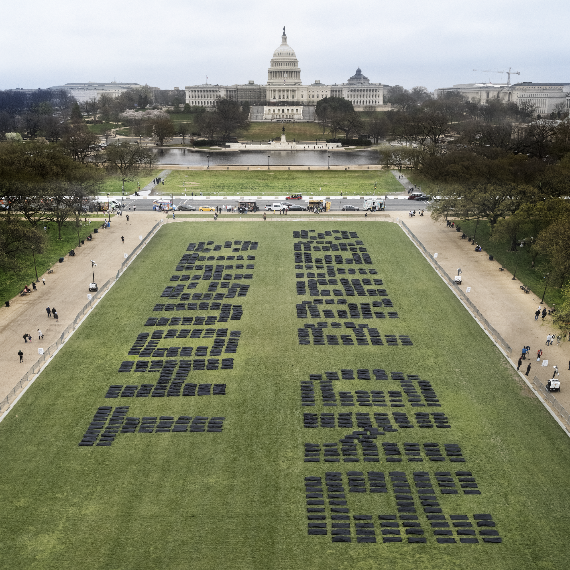 Body bags laid on the ground spell out "thoughts and prayers."