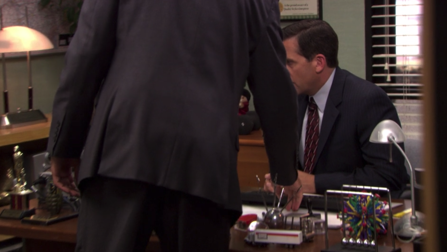 A man (John Krasinski as Jim Halpert on "The Office") turning down the volume on another man's (Steve Carell as Michael Scott) computer.
