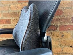 Grey cushion on black desk chair in front of brick wall