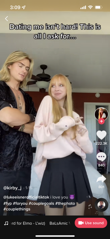 Screenshot of TikTok video showing a white man and woman standing next to each other, with the woman leaning into the man to flirt.