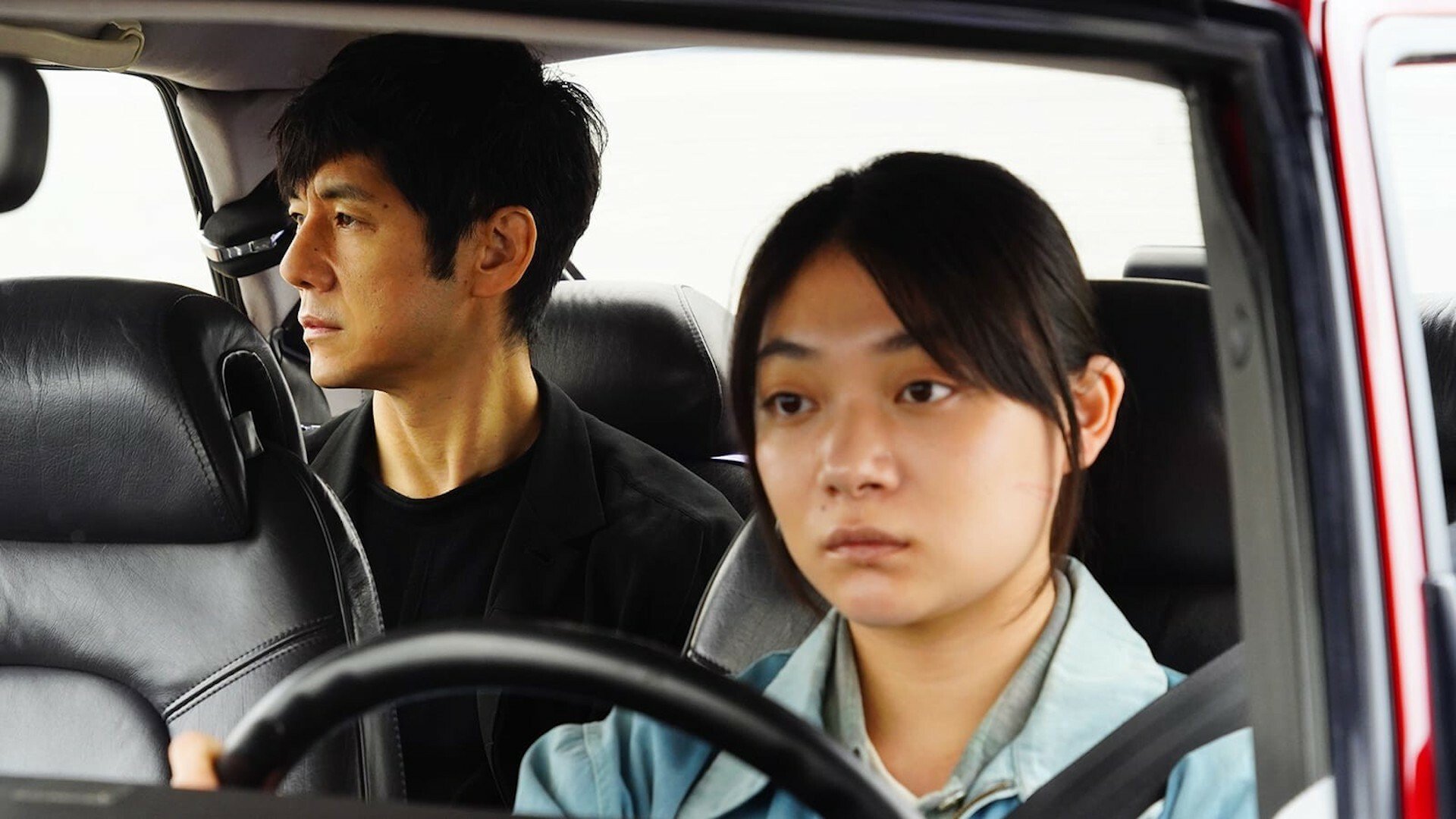 Tôko Miura drives a car while Hidetoshi Nishijima sits in the back in the film "Drive My Car."