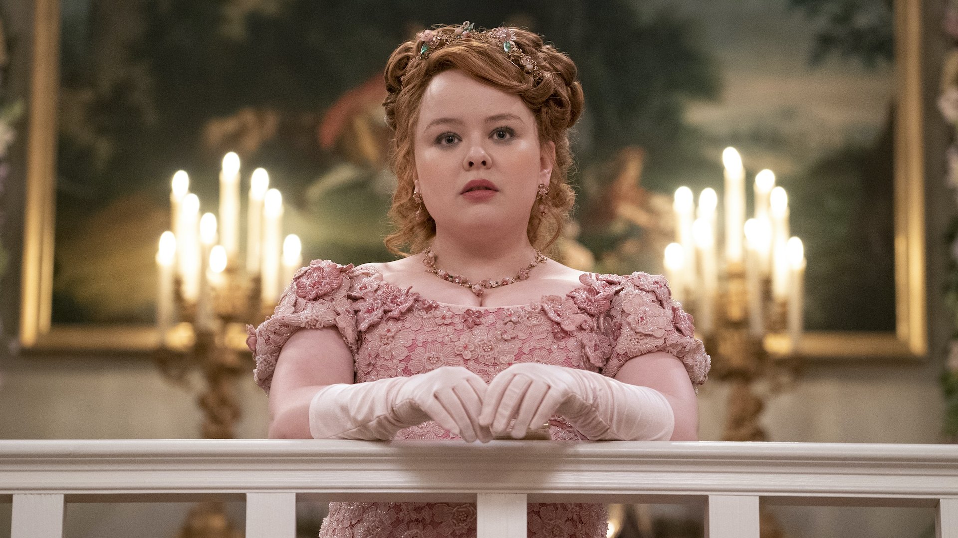 A young woman in a pink Regency gown stands against a banister; still from "Bridgerton."