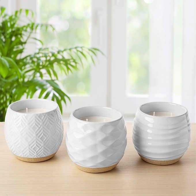 Three candles in white jars on wooden table