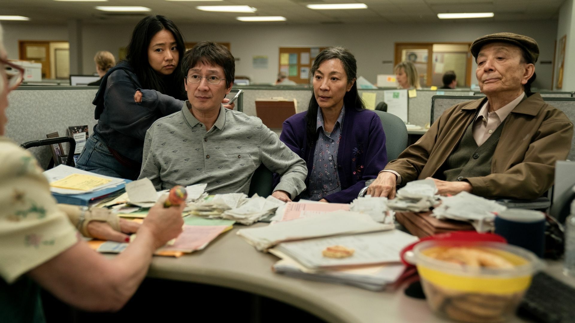 An Asian family sits in a cubicle, huddled over a desk full of receipts.