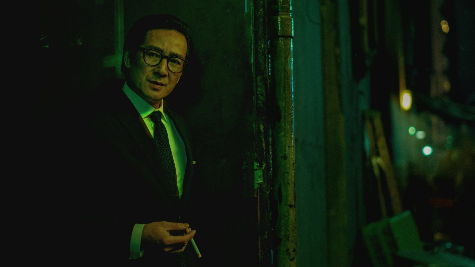 A dashing Asian man holds a lit cigarette.