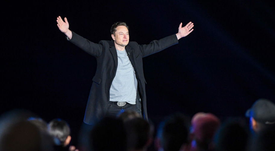 Elon Musk stands in front of a crowd.