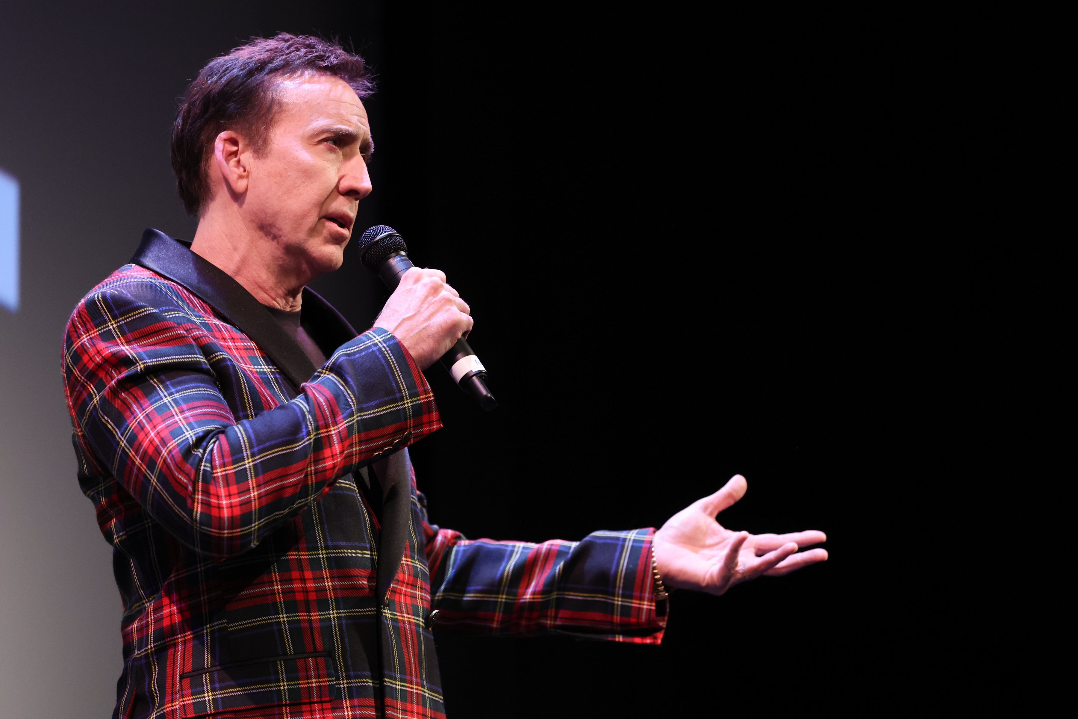 Nicolas Cage holds a microphone and speaks to a crowd.