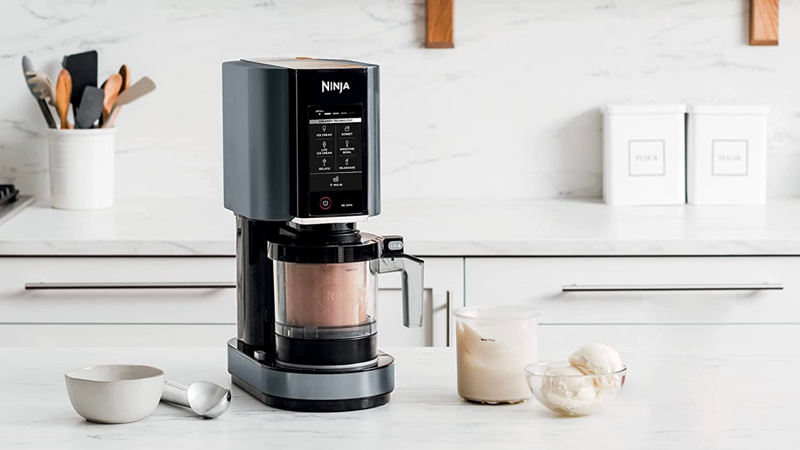 the ninja creami next to some bowls of ice cream on a white marble countertop