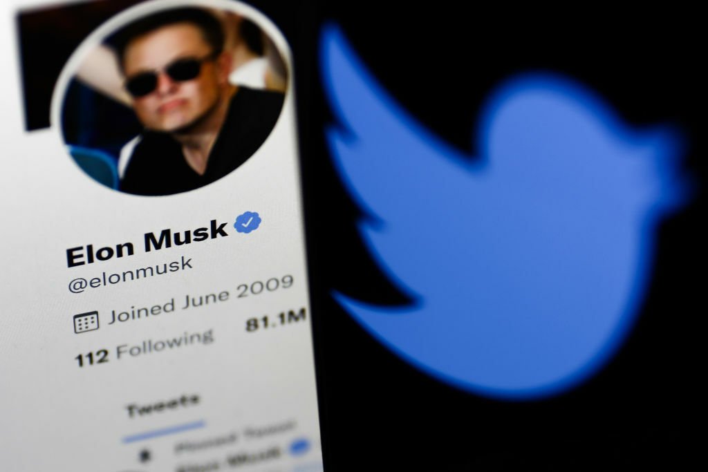 Elon Musk's Twitter profile displayed on a computer screen and Twitter logo displayed on a phone screen