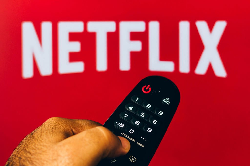 Hand holding a remote in front of a Netflix logo.