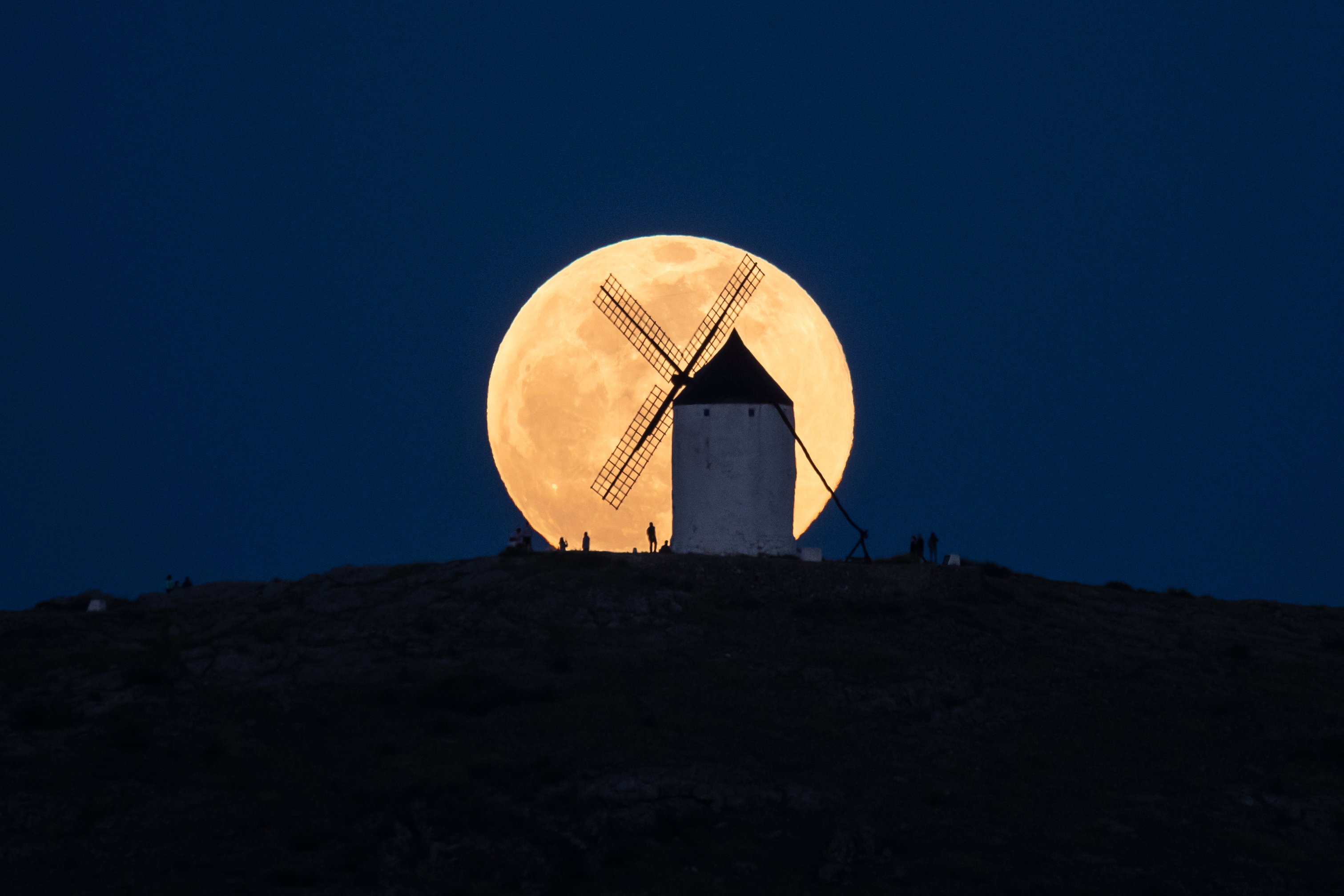 A windmill silhouetted against a large full moon.