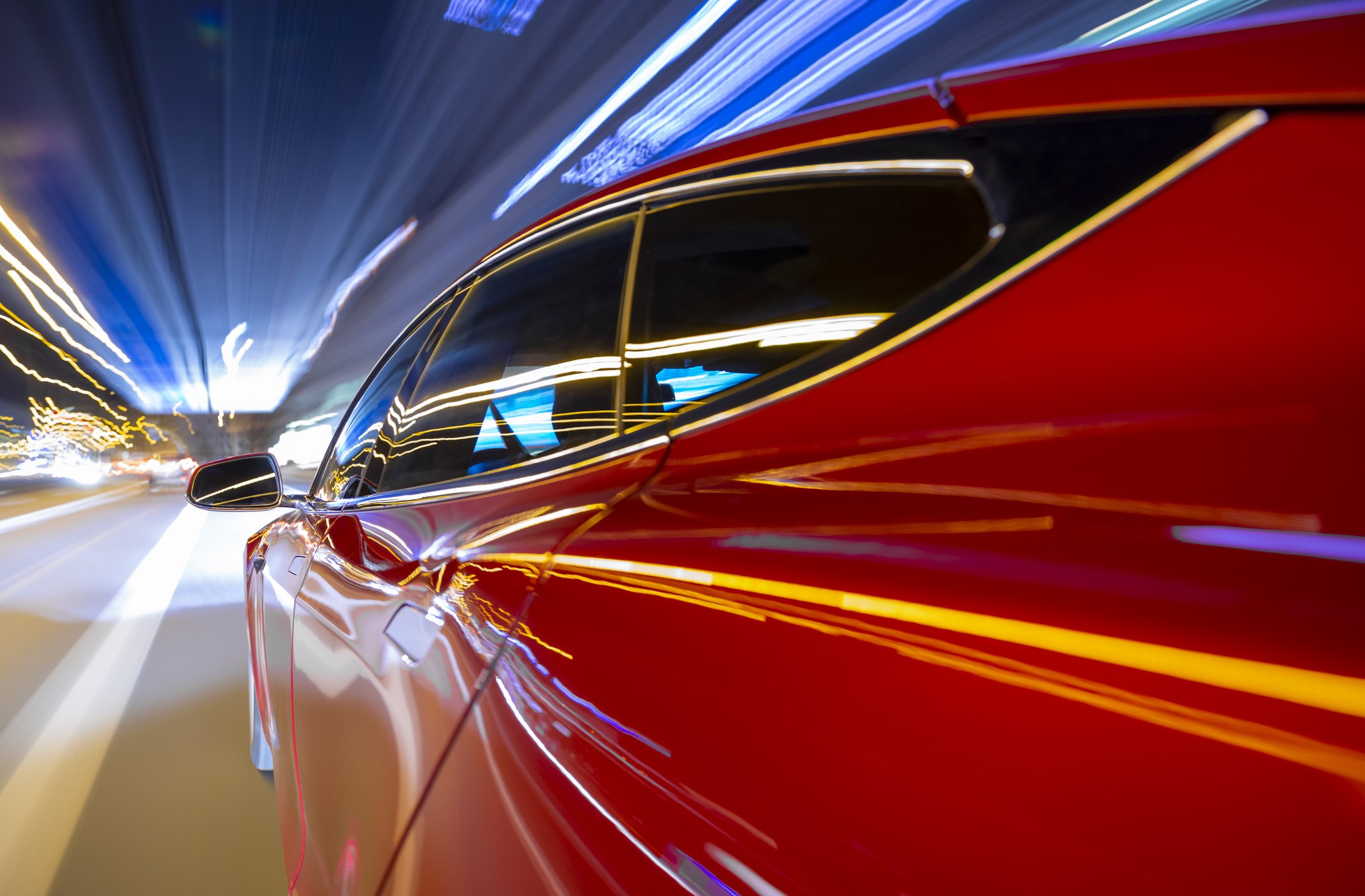 Red car driving fast at night alongside street lights