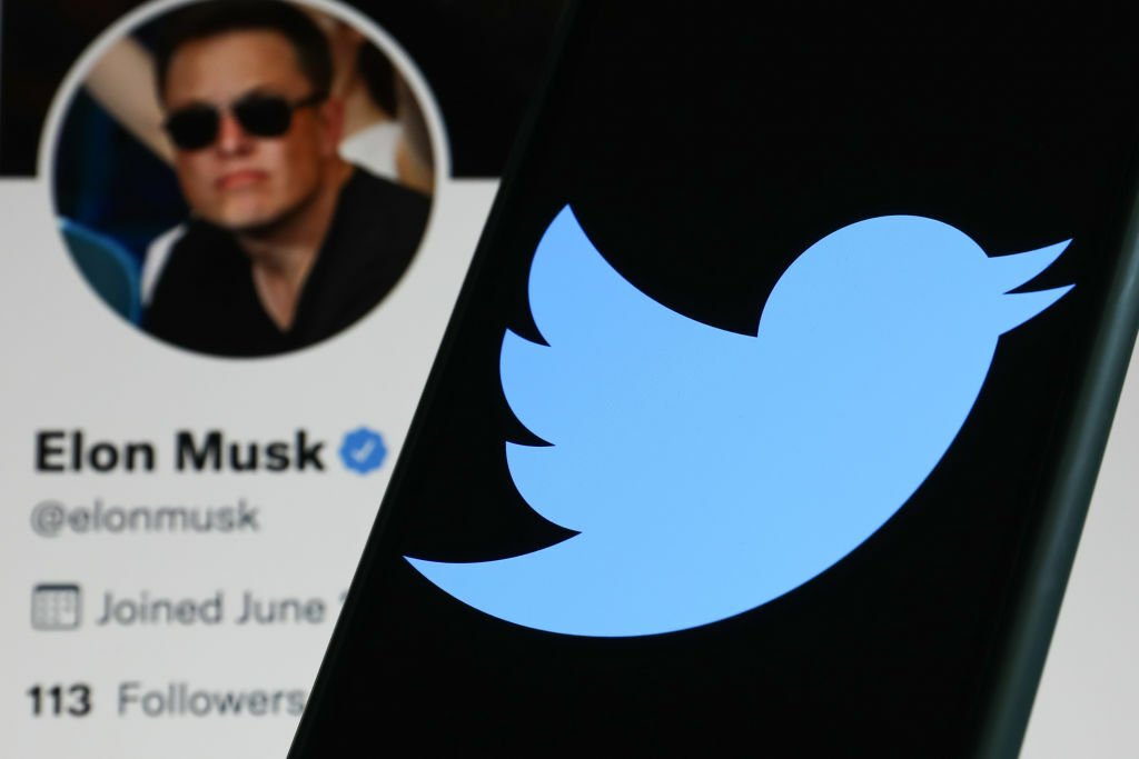 Elon Musk twitter page next to phone displaying Twitter logo