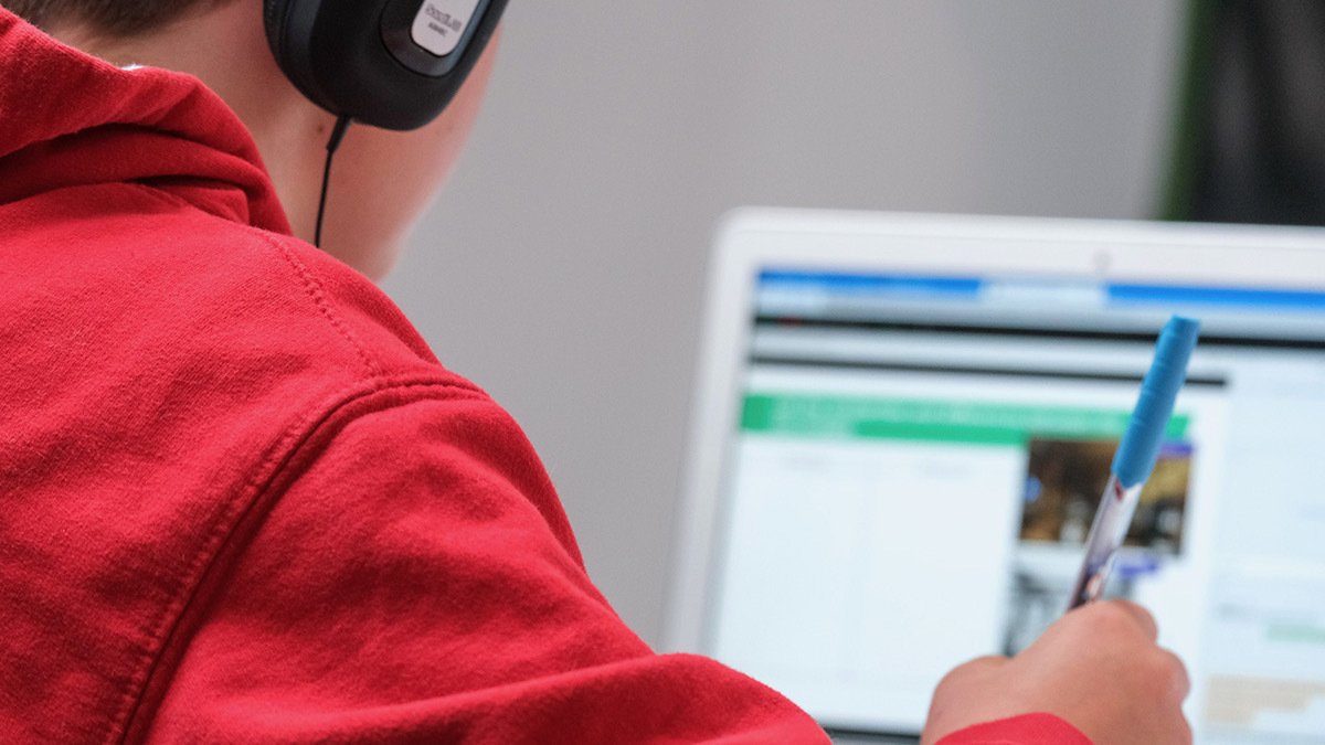 Person wearing headphones and holding pen looking at laptop screen