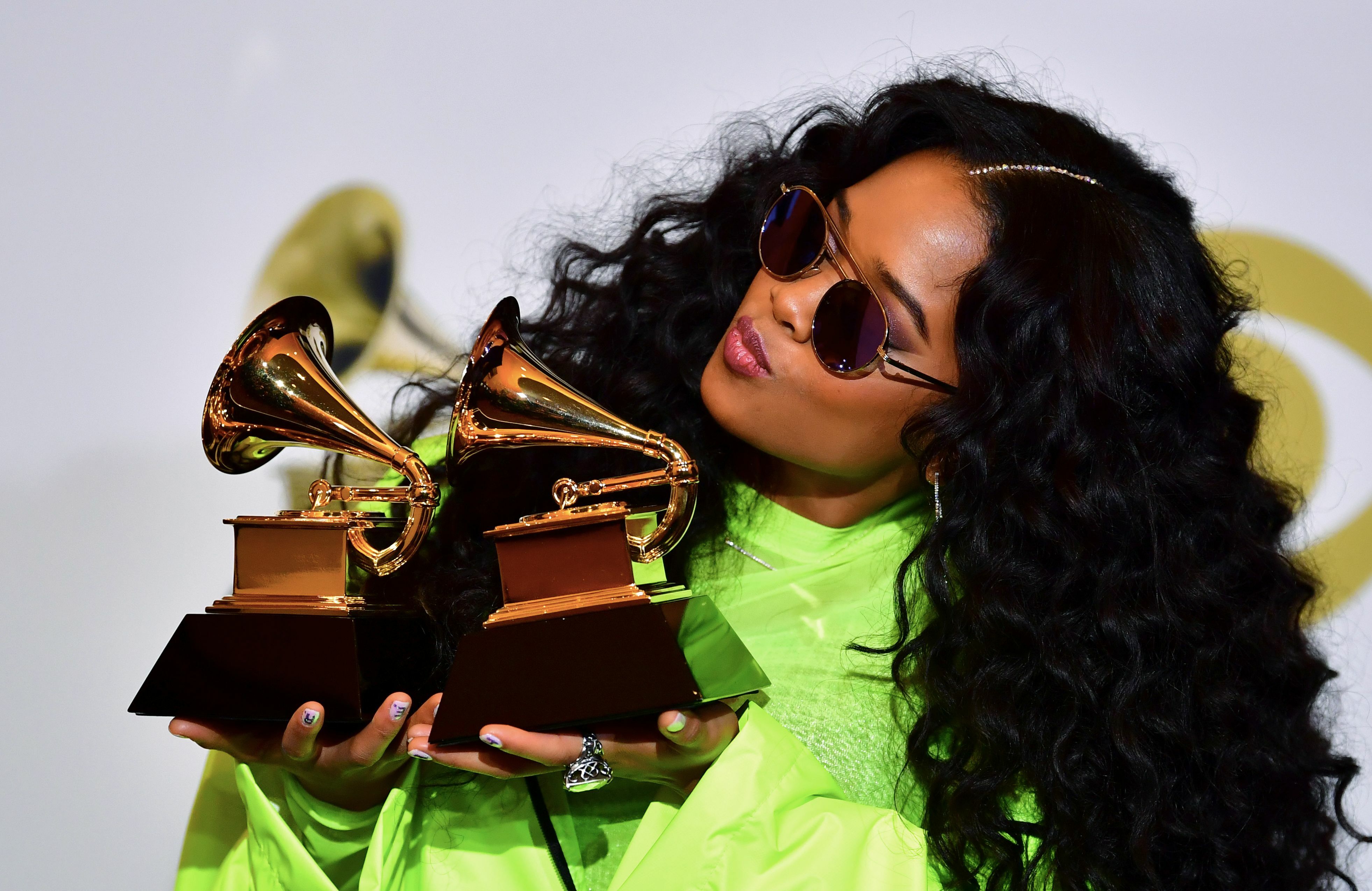 Singer H.E.R. poses wearing sunglasses and a fluorescent green dress with Grammy Awards in 2019. 