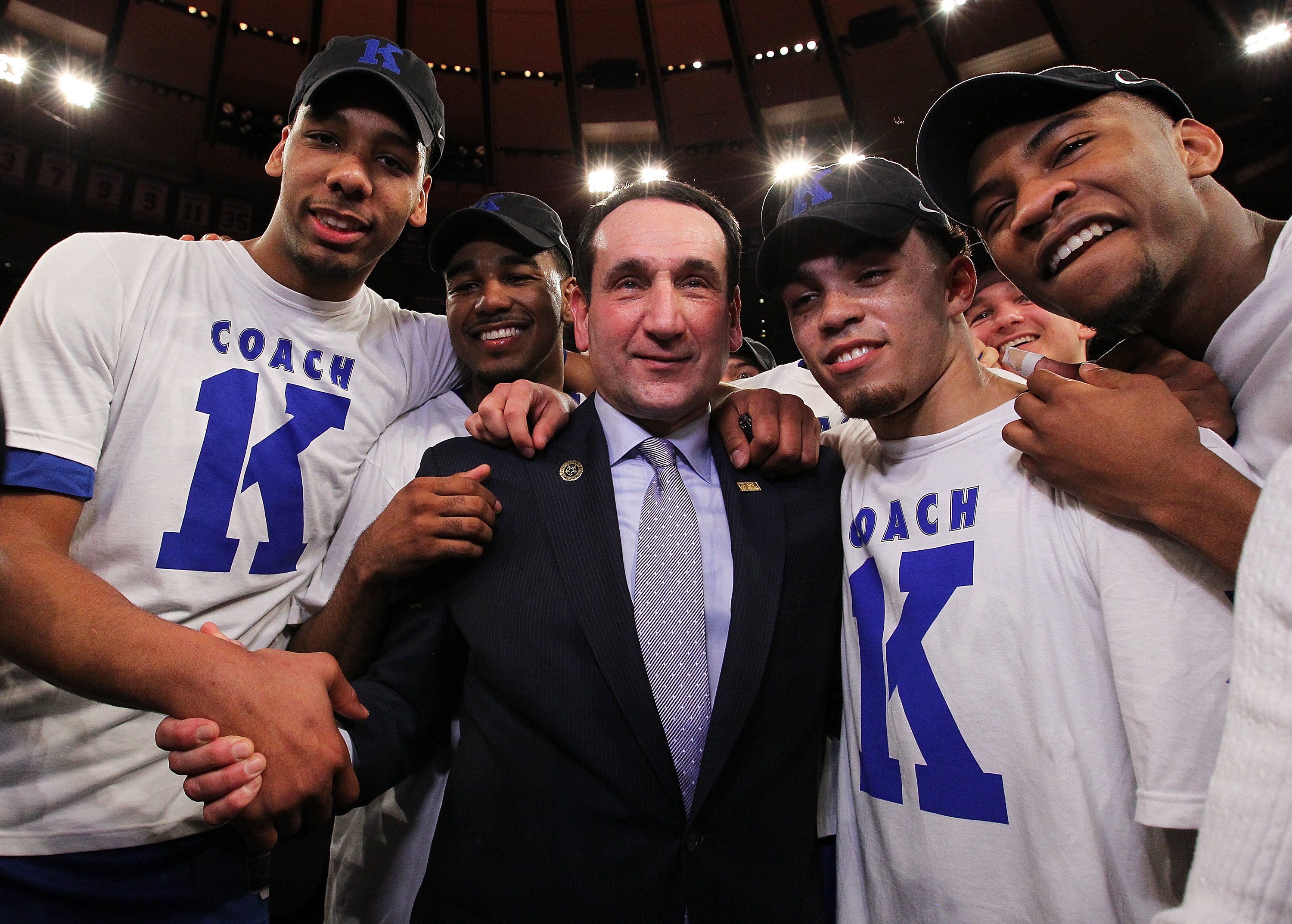Duke head coach Mike Krzyzewski of the Duke Blue Devils leans forward, apparently shouting, with fists clenched. 