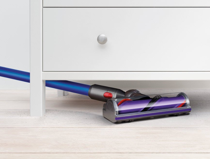 Dyson V10 Allergy cordless vacuum cleaning dirt from underneath a white dresser